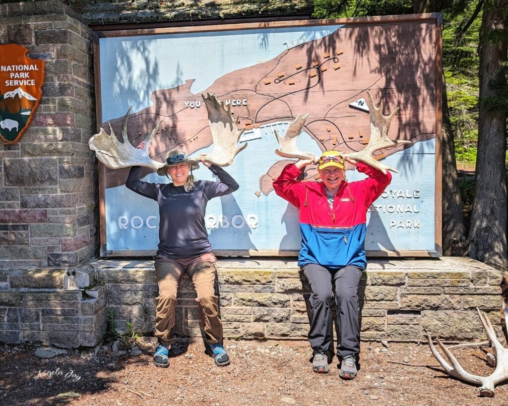 two women holding moose antlers by the Isle Royale sign