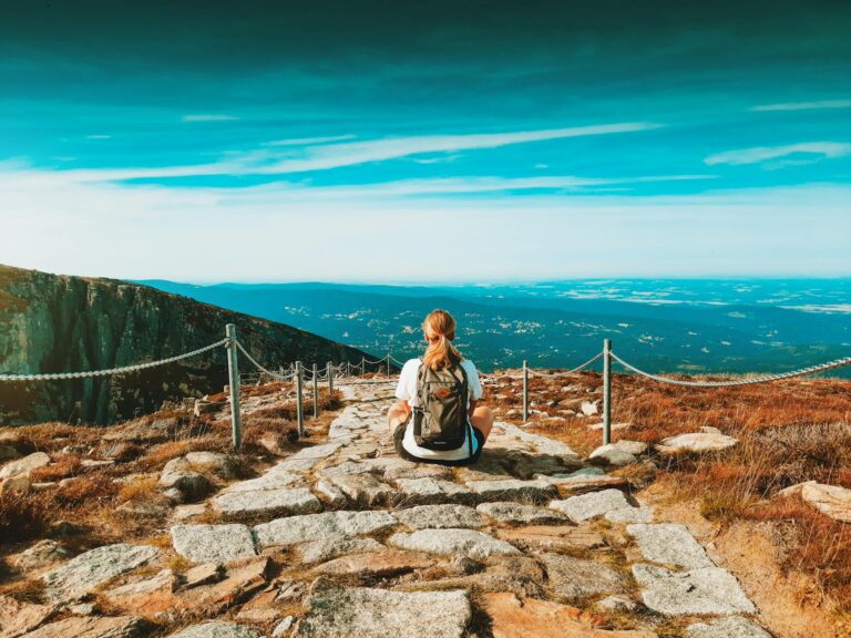 blonde woman sitting on rocky footpath in mountains