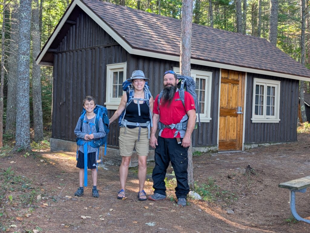 A family with backpacks standing outside of the Twelve Mile Beach cabin in Pictured Rocks National Lakeshore